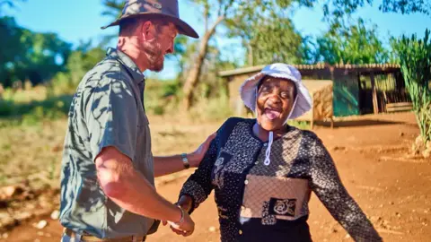 AFP via Getty Images Miriam Mupambawashe (R) in a white hat laughs as she shakes hands with Daniel Burger (R) wearing a white-brimmed brown hat near Sherwood Park Estates Farm in Kwekwe, Zimbabwe - May 2025