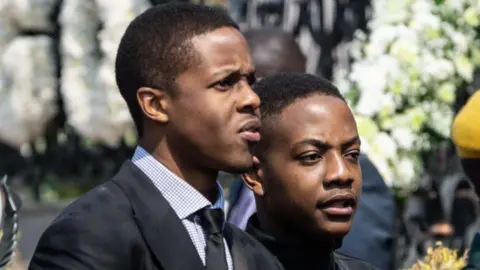 AFP via Getty Images Robert Mugabe's son, Robert Jr and Bellarmine, are seen standing next to one another in black suits